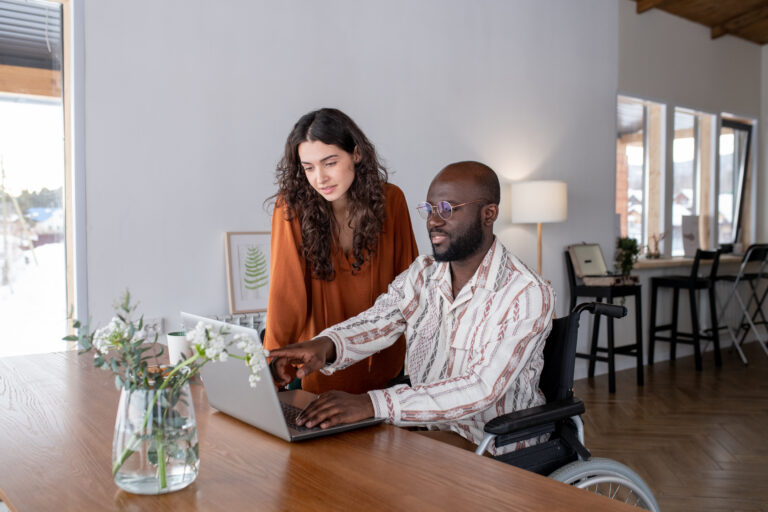 Young African American man with disability pointing at laptop screen during presentation of new project to Caucasian female colleague