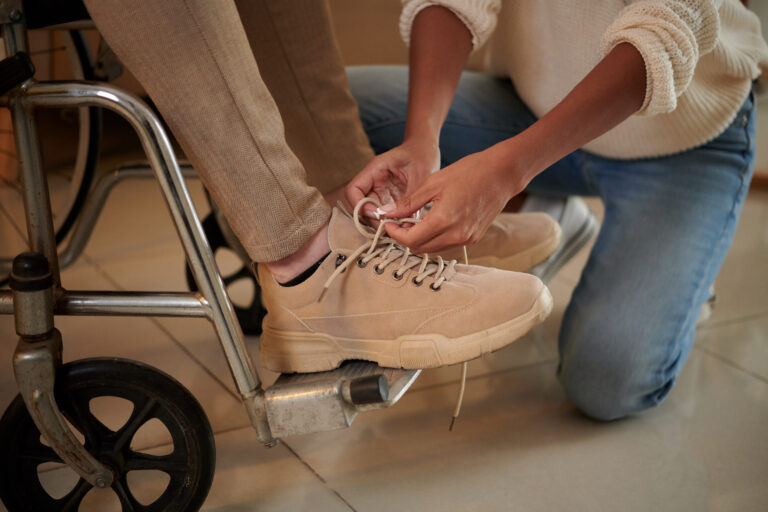 Closeup image of young woman tying shoe laces of boyfriend sitting in wheelchair